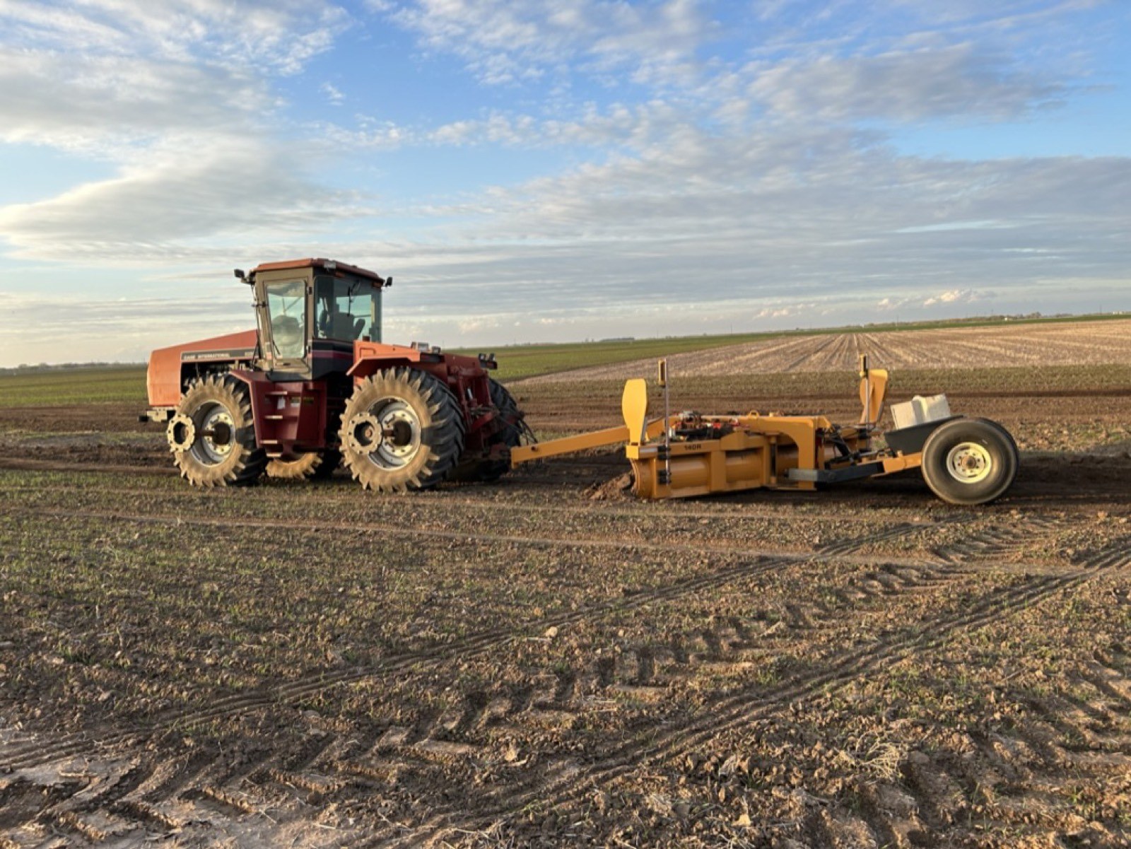 Tractor pulling a grader blade across a field
